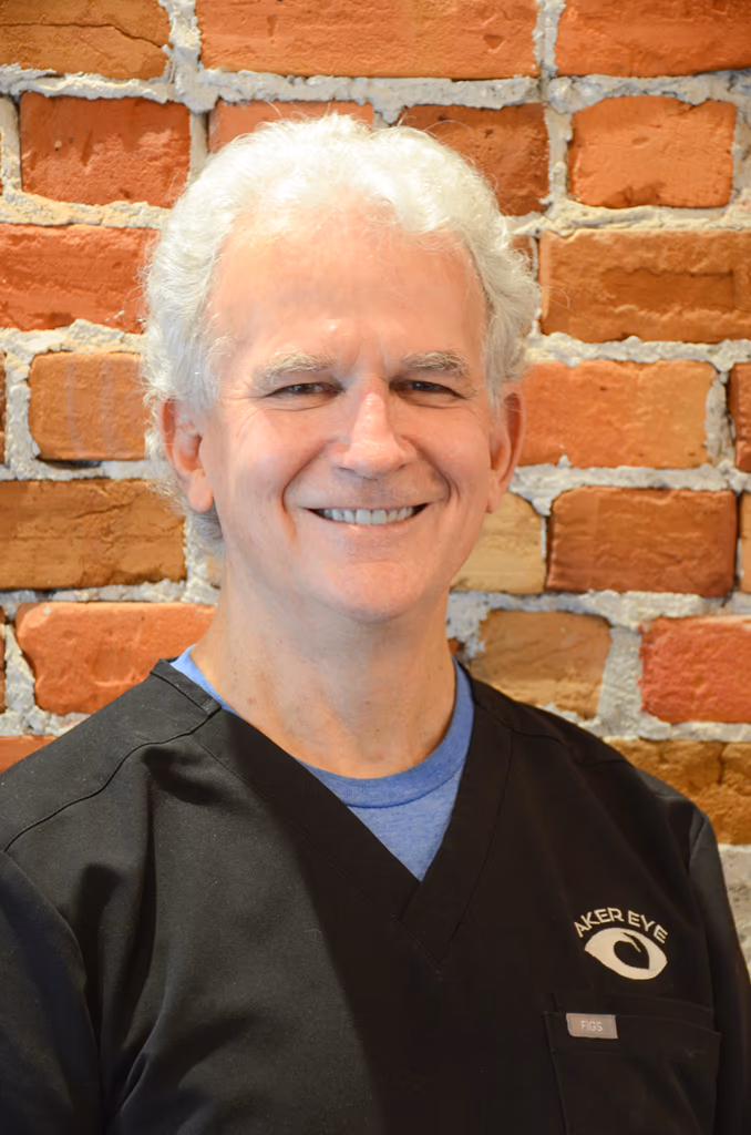 Dr. Greg Aker, optometrist at Aker Eye in Titusville, smiling in black scrubs in front of a brick wall