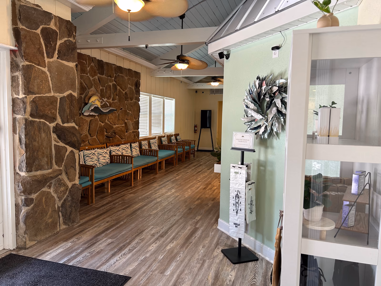 The waiting room at Aker Eye Playalinda, 1114 S Washington Ave, Titusville: a stone wall with a wave sculpture and teak chairs with teal cushions